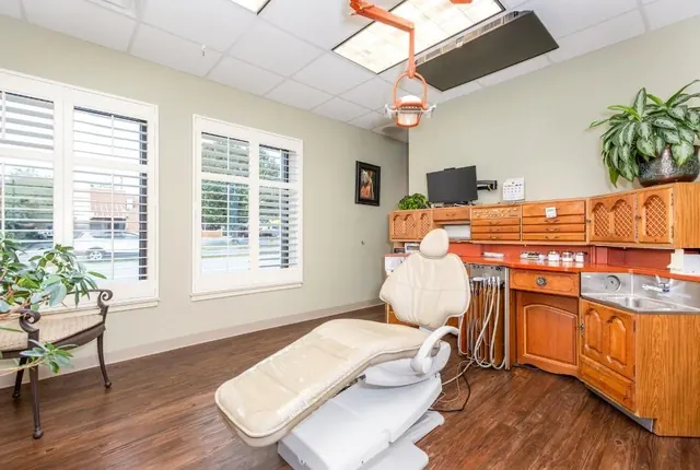 A treatment room with a dental chair, wooden cabinets and a ceiling-mounted screen.
