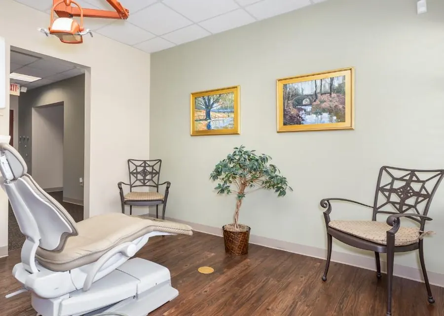 A bright treatment room with a dental chair and two armchairs.